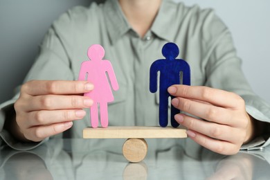 Gender equality concept. Woman with male and female figures on scales at grey table, closeup