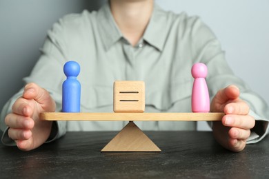 Gender equality concept. Woman with male and female figures on scales at dark table, closeup