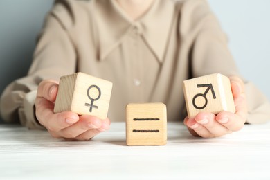 Gender equality concept. Woman with wooden cubes of male and female symbols at white table, closeup