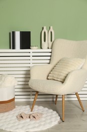 Photo of Beige armchair with soft pillow, slippers and different decorative elements indoors