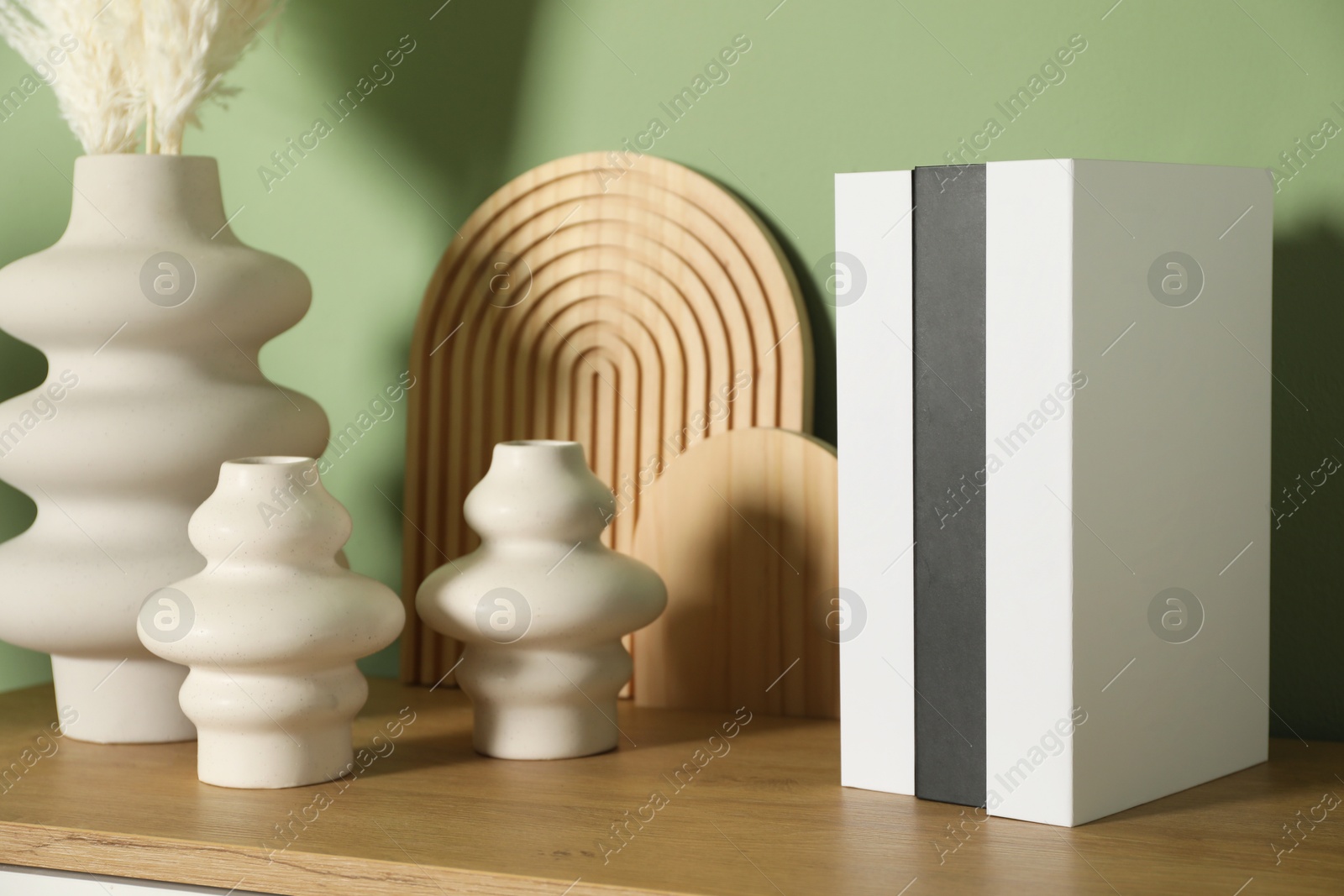 Photo of Beautiful decorative plants, vases, wooden boards and hardcover books with different cities names on table near green wall indoors