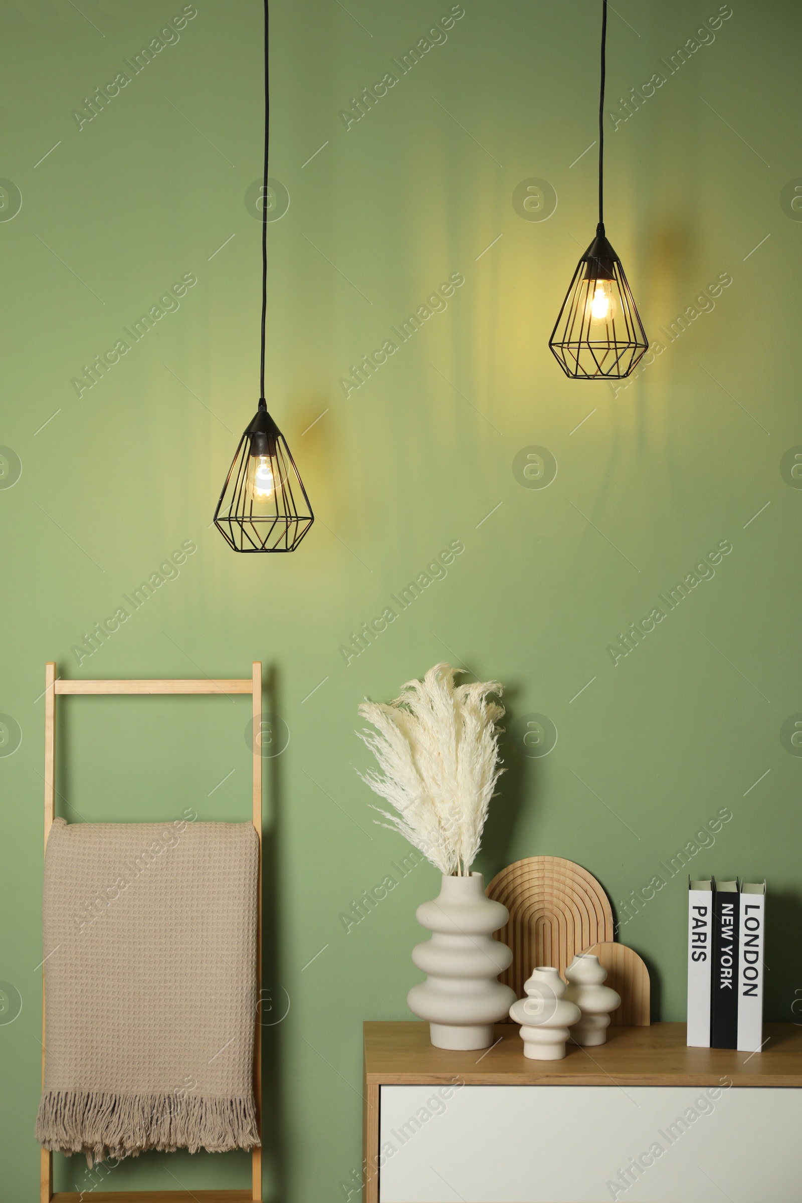 Photo of Different decorative elements on chest of drawers and blanket near green wall indoors