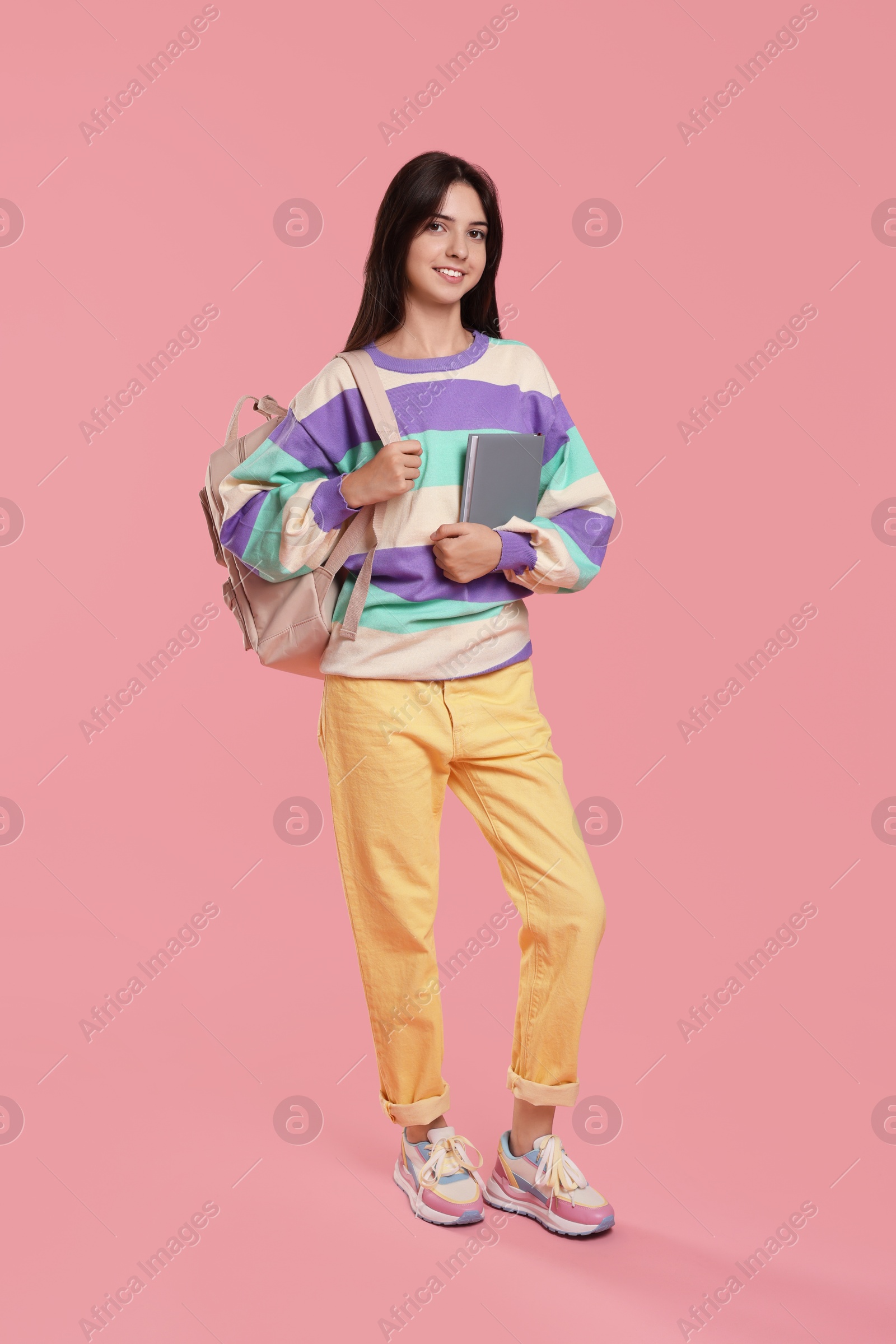 Photo of Cute teenage girl with backpack and book on pink background