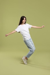 Cheerful teenage girl dancing on olive background