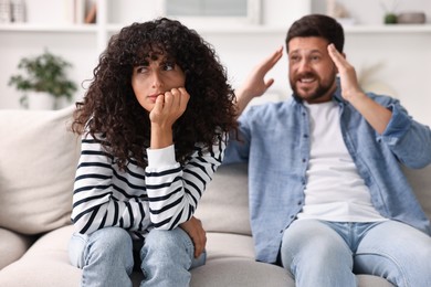 Emotional couple having quarrel on sofa at home, selective focus. Relationship problems