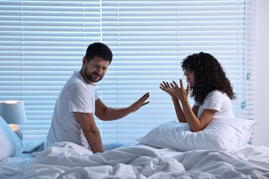 Photo of Emotional couple arguing in bedroom at night. Relationship problems