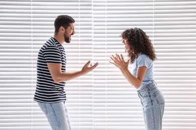 Photo of Emotional couple arguing against white blinds. Relationship problems