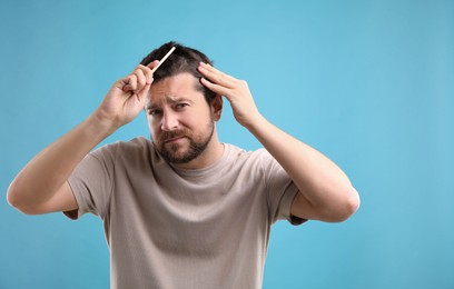 Photo of Man brushing his hair on light blue background, space for text. Alopecia problem