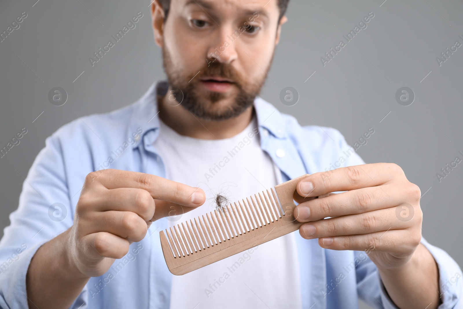 Photo of Sad man taking his lost hair from comb on gray background, closeup. Alopecia problem