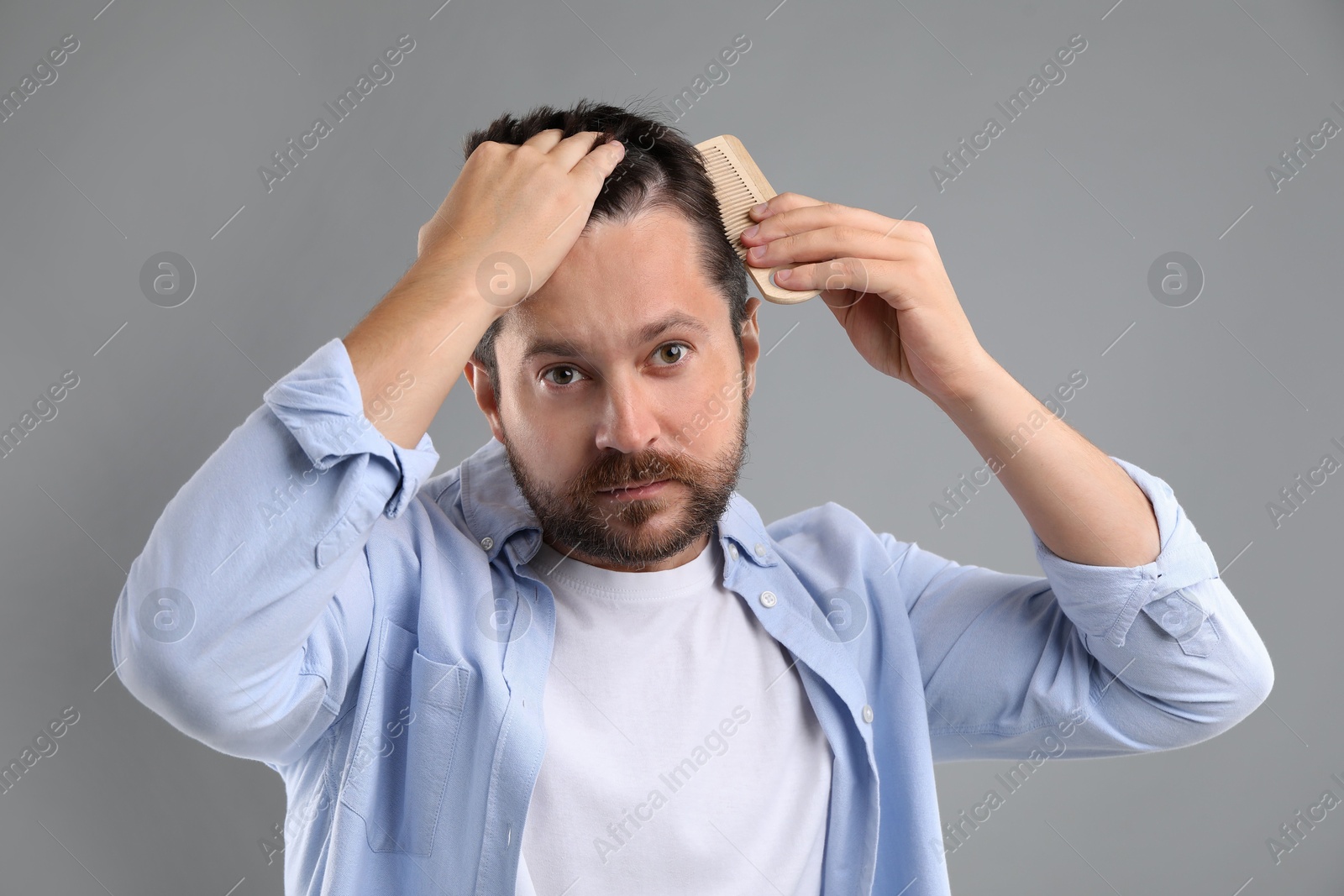 Photo of Man brushing his hair on gray background. Alopecia problem