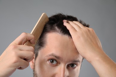 Photo of Man brushing his hair on gray background, closeup. Alopecia problem