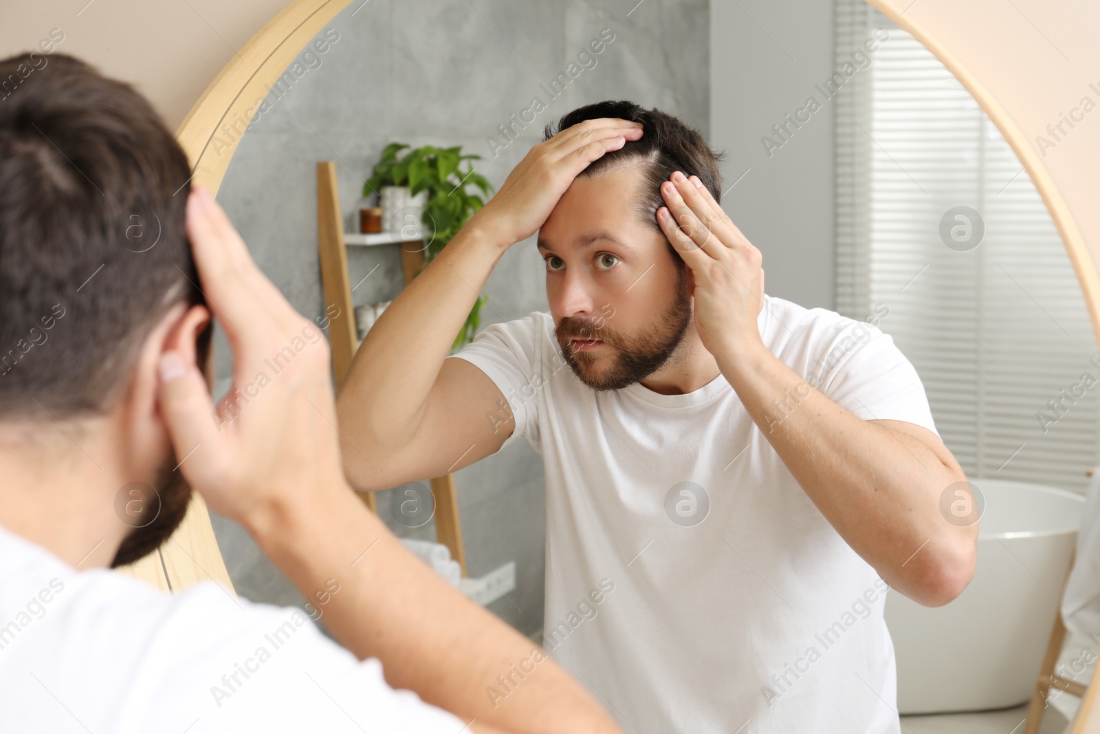 Photo of Man with hair loss problem looking at mirror indoors