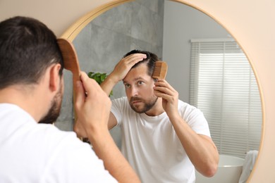 Man brushing his hair near mirror indoors. Alopecia problem