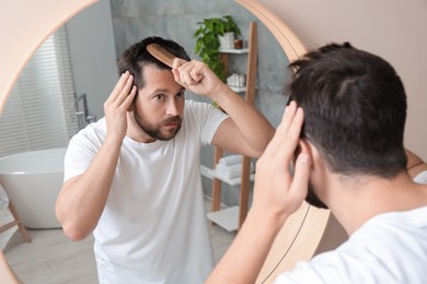 Photo of Man brushing his hair near mirror indoors. Alopecia problem