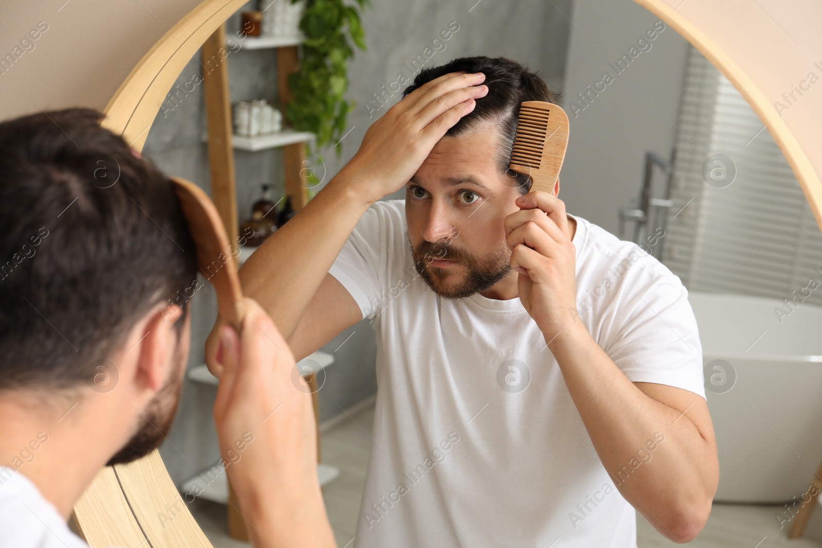 Photo of Man brushing his hair near mirror indoors. Alopecia problem