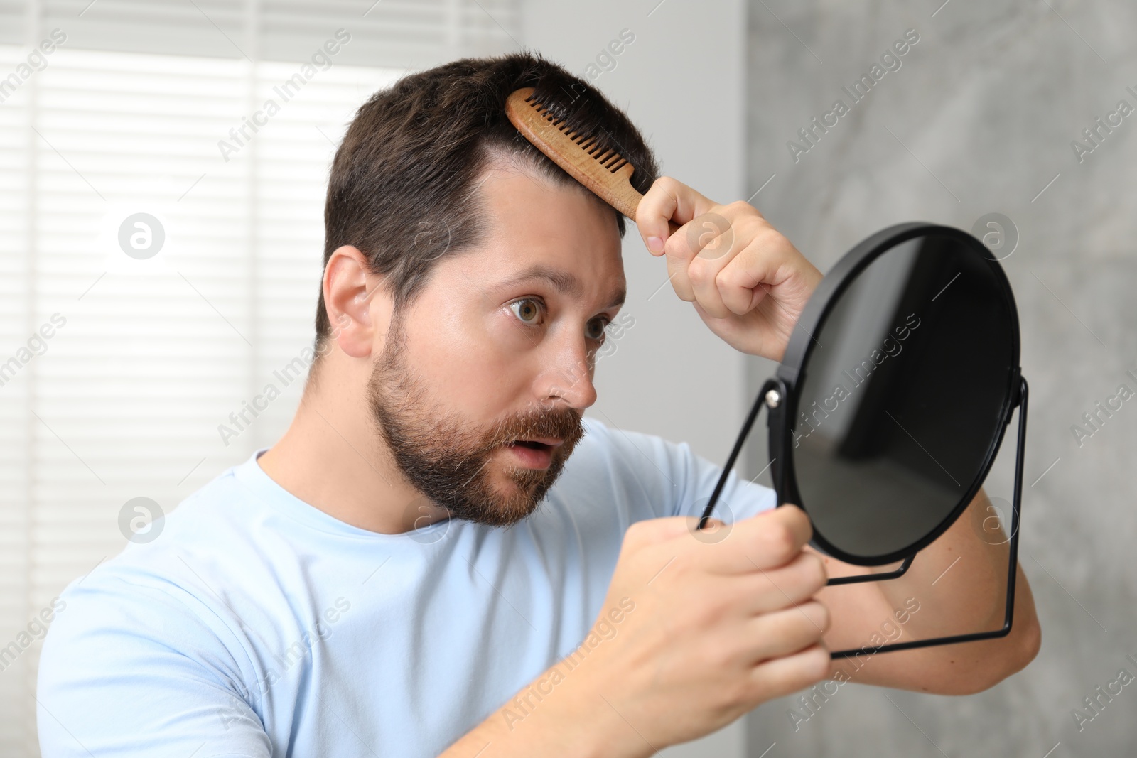 Photo of Man brushing his hair near mirror indoors. Alopecia problem