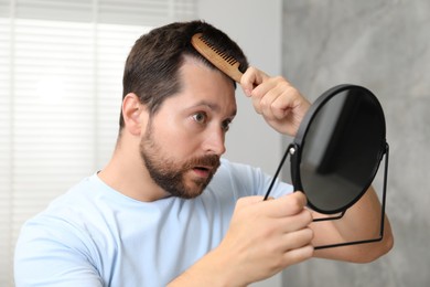 Man brushing his hair near mirror indoors. Alopecia problem