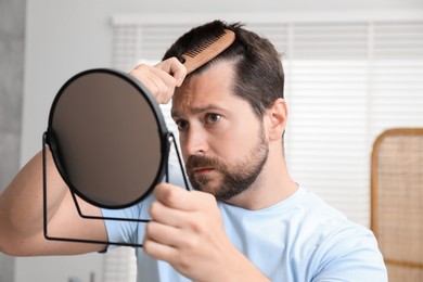 Man brushing his hair near mirror indoors. Alopecia problem