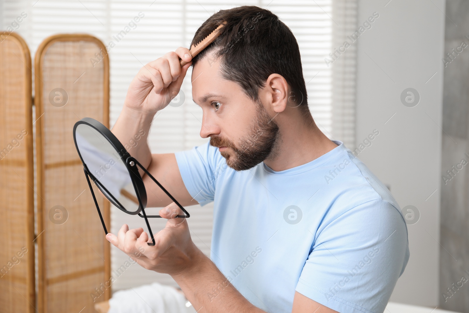 Photo of Man brushing his hair near mirror indoors. Alopecia problem