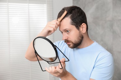 Photo of Man brushing his hair near mirror indoors. Alopecia problem