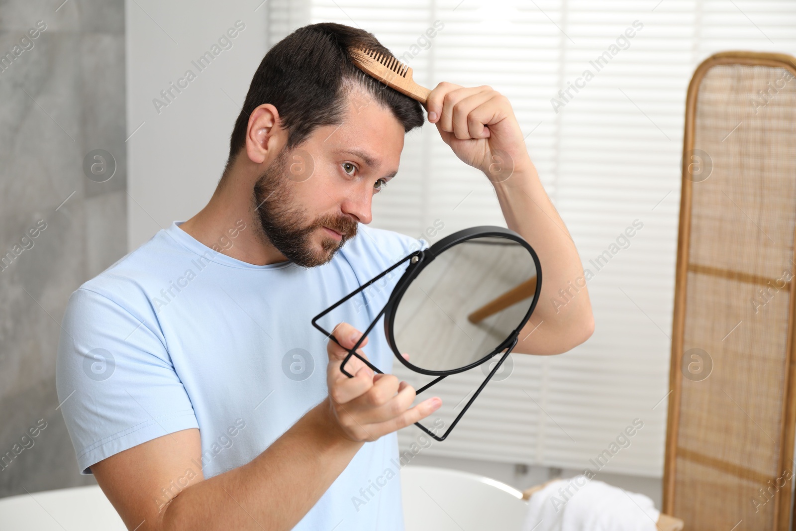 Photo of Man brushing his hair near mirror indoors. Alopecia problem