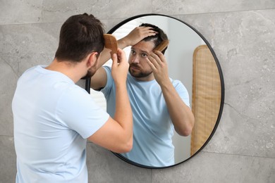 Man brushing his hair near mirror indoors. Alopecia problem