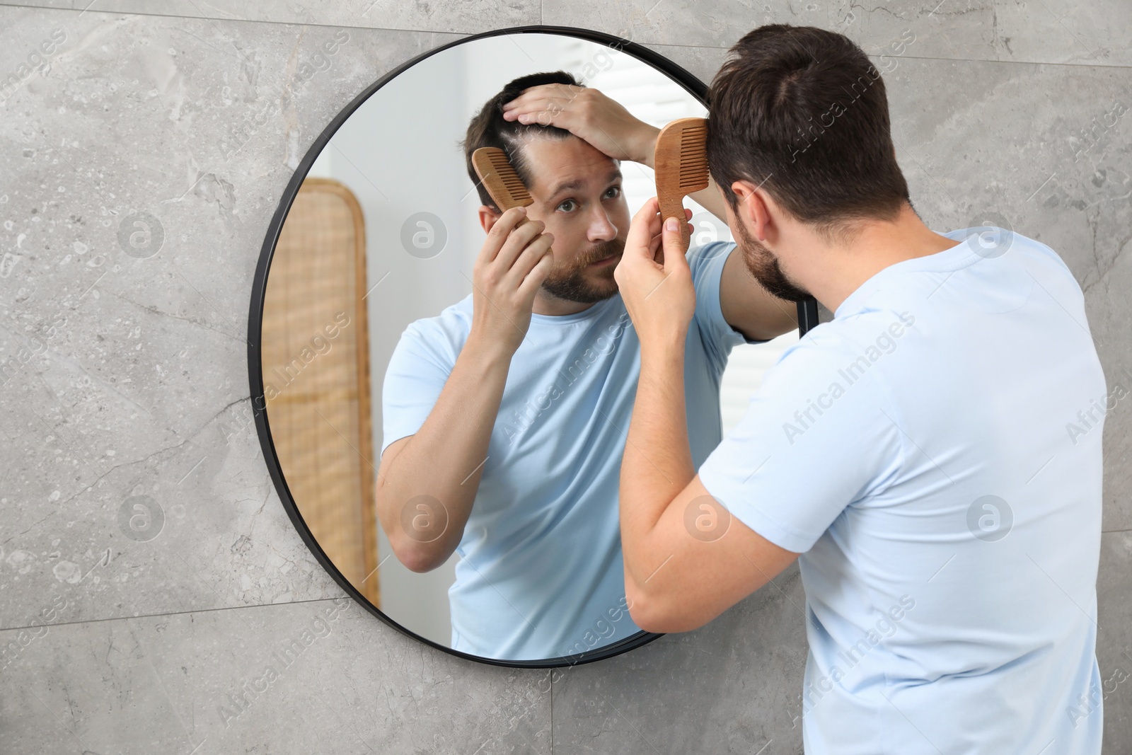 Photo of Man brushing his hair near mirror indoors. Alopecia problem