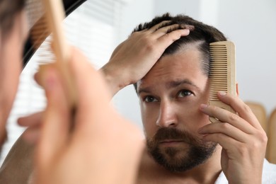 Man brushing his hair near mirror indoors. Alopecia problem