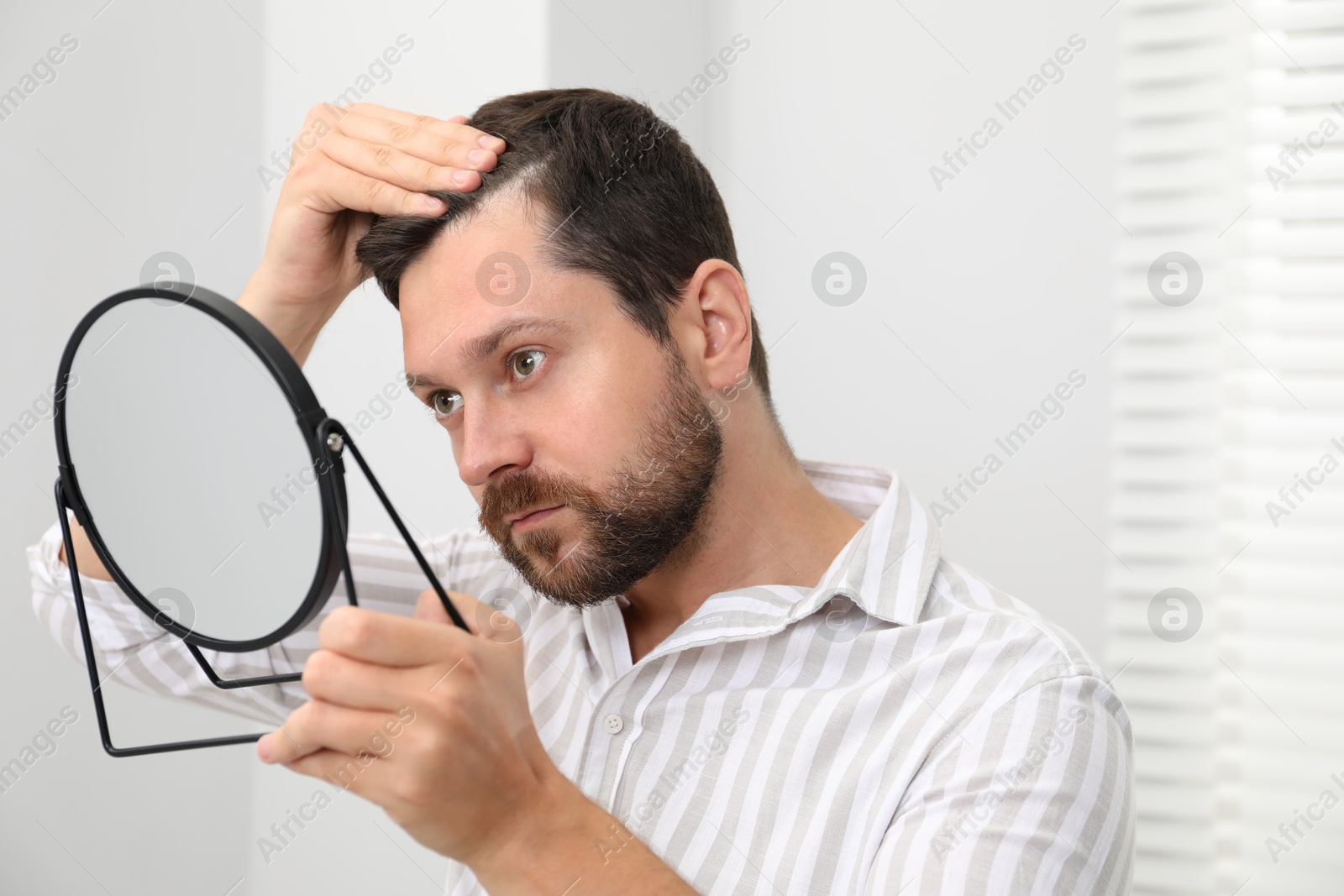 Photo of Man with hair loss problem looking at mirror indoors