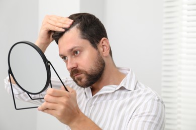 Photo of Man with hair loss problem looking at mirror indoors