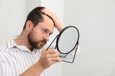 Man with hair loss problem looking at mirror indoors