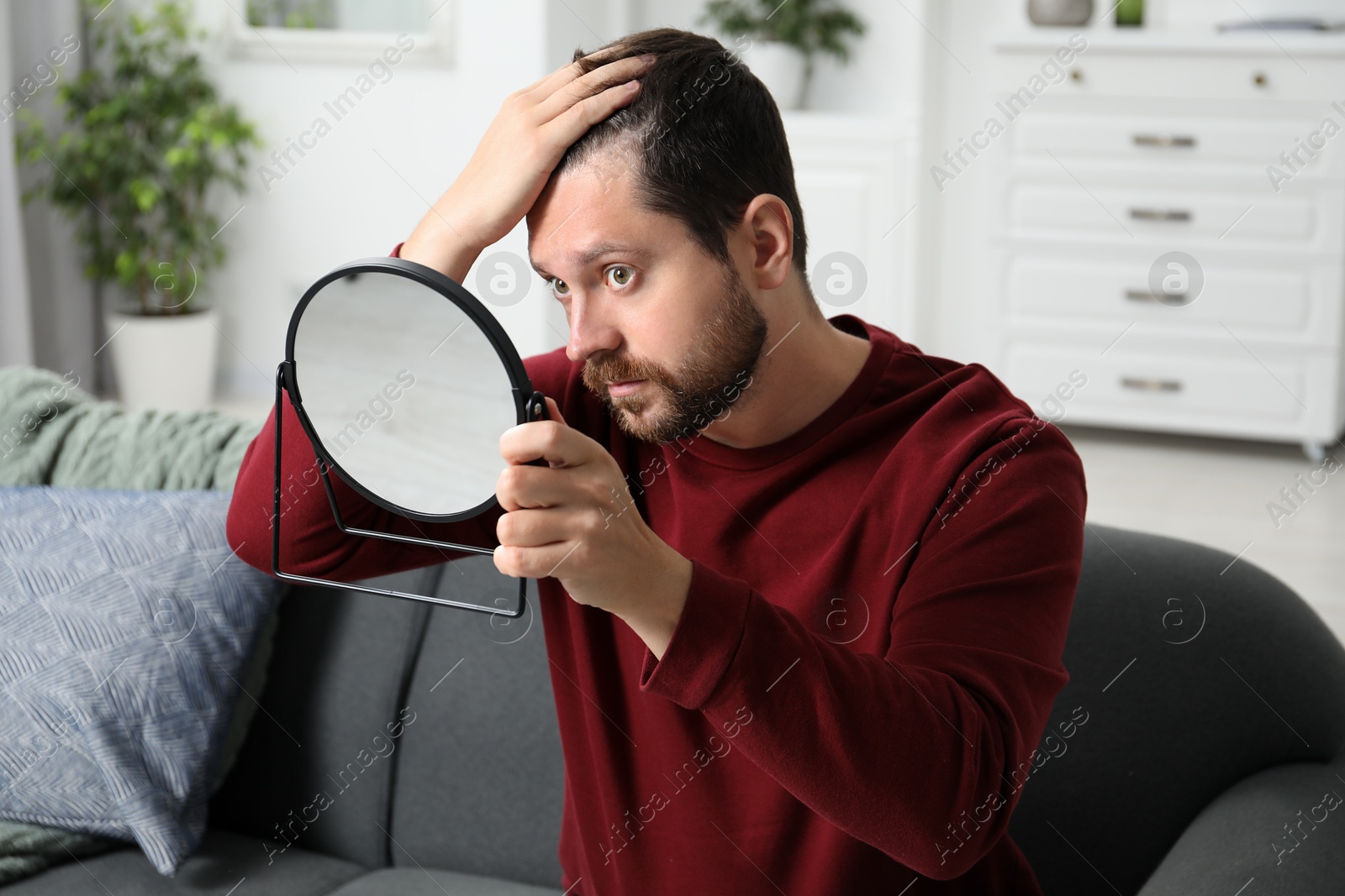 Photo of Man with hair loss problem looking at mirror indoors