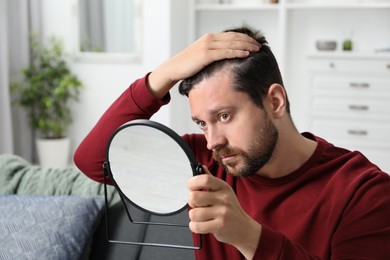 Photo of Man with hair loss problem looking at mirror indoors