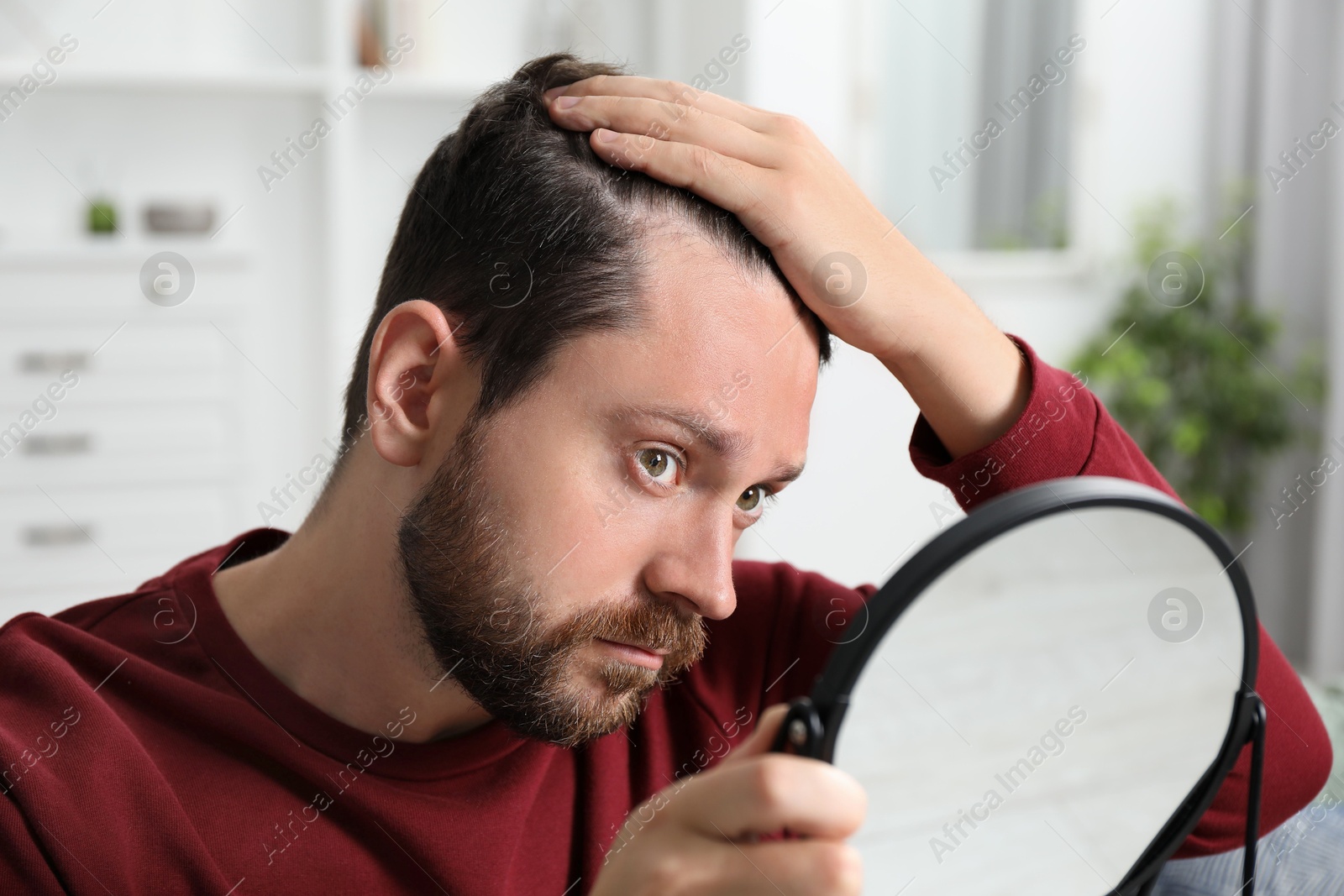 Photo of Man with hair loss problem looking at mirror indoors