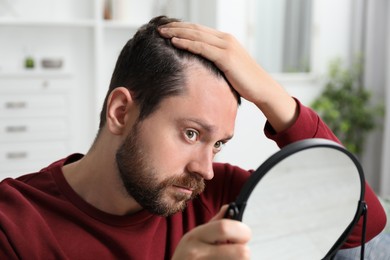 Photo of Man with hair loss problem looking at mirror indoors