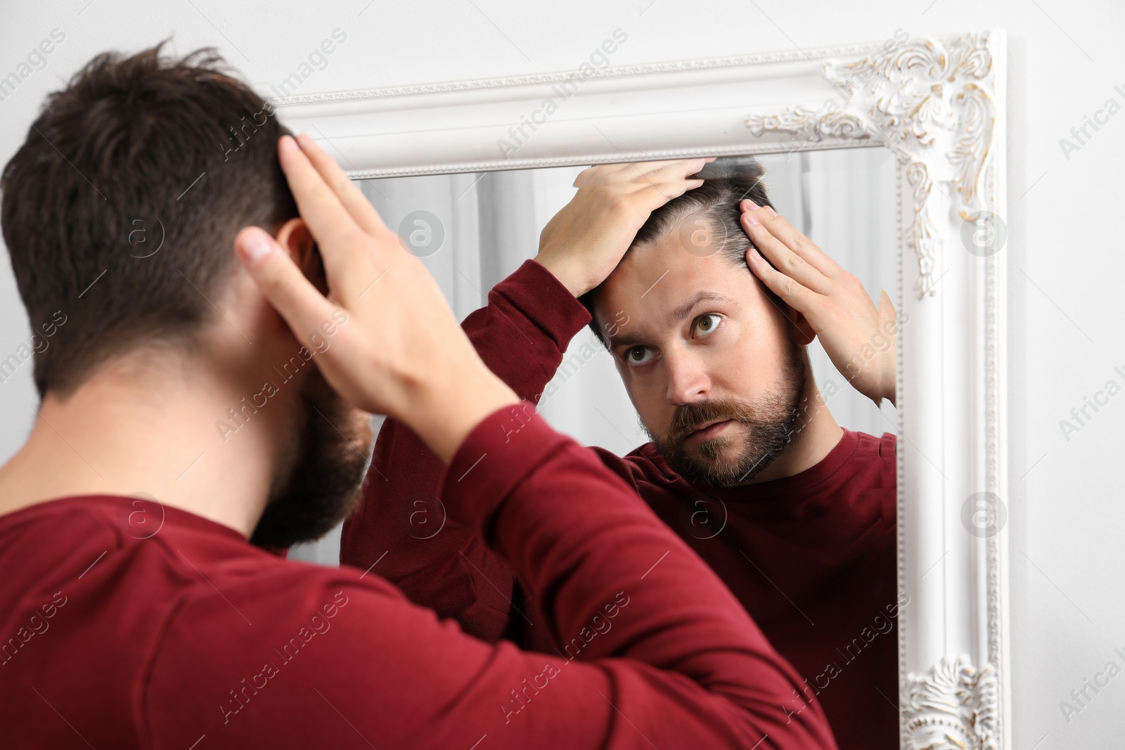 Photo of Man with hair loss problem looking at mirror indoors