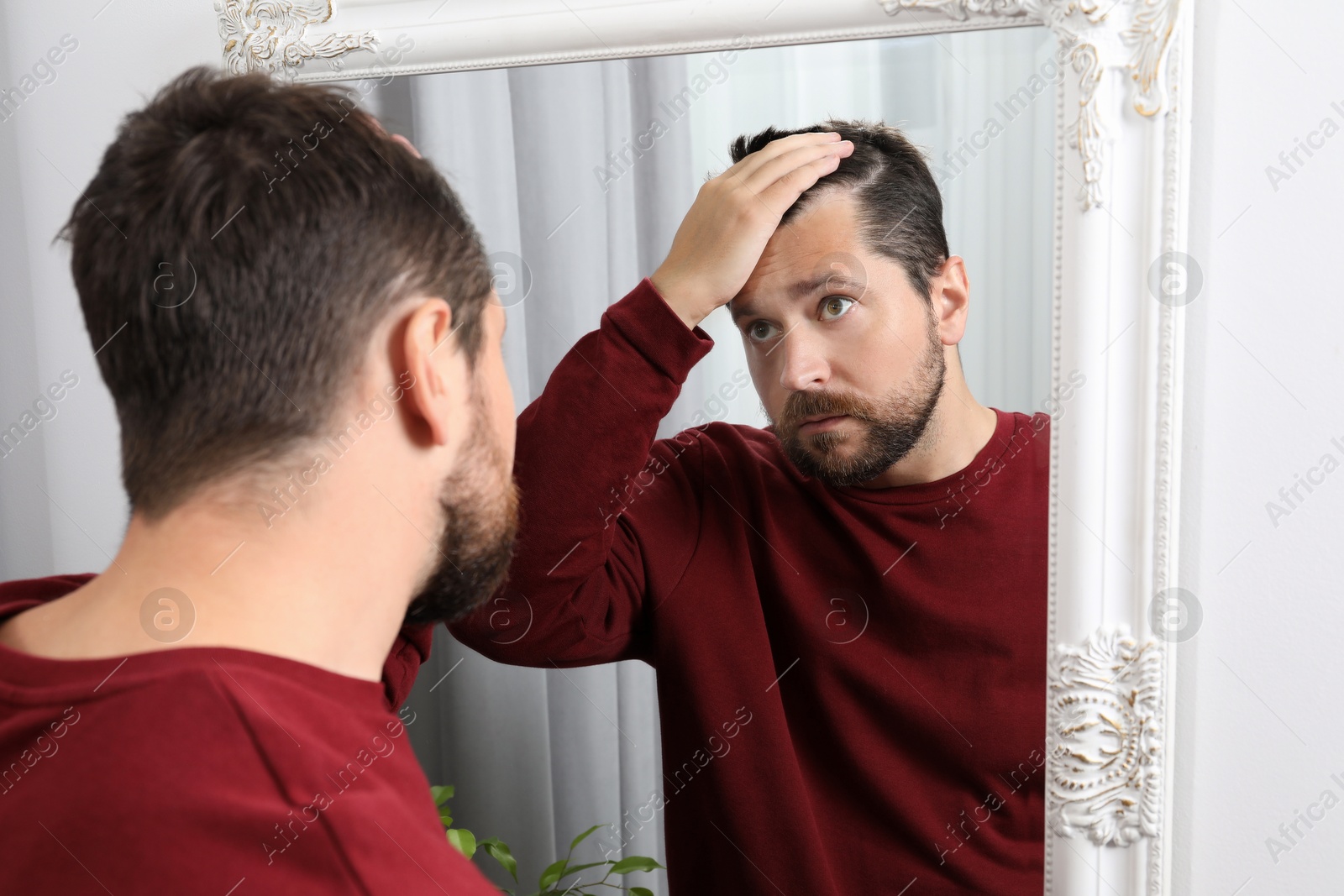 Photo of Man with hair loss problem looking at mirror indoors