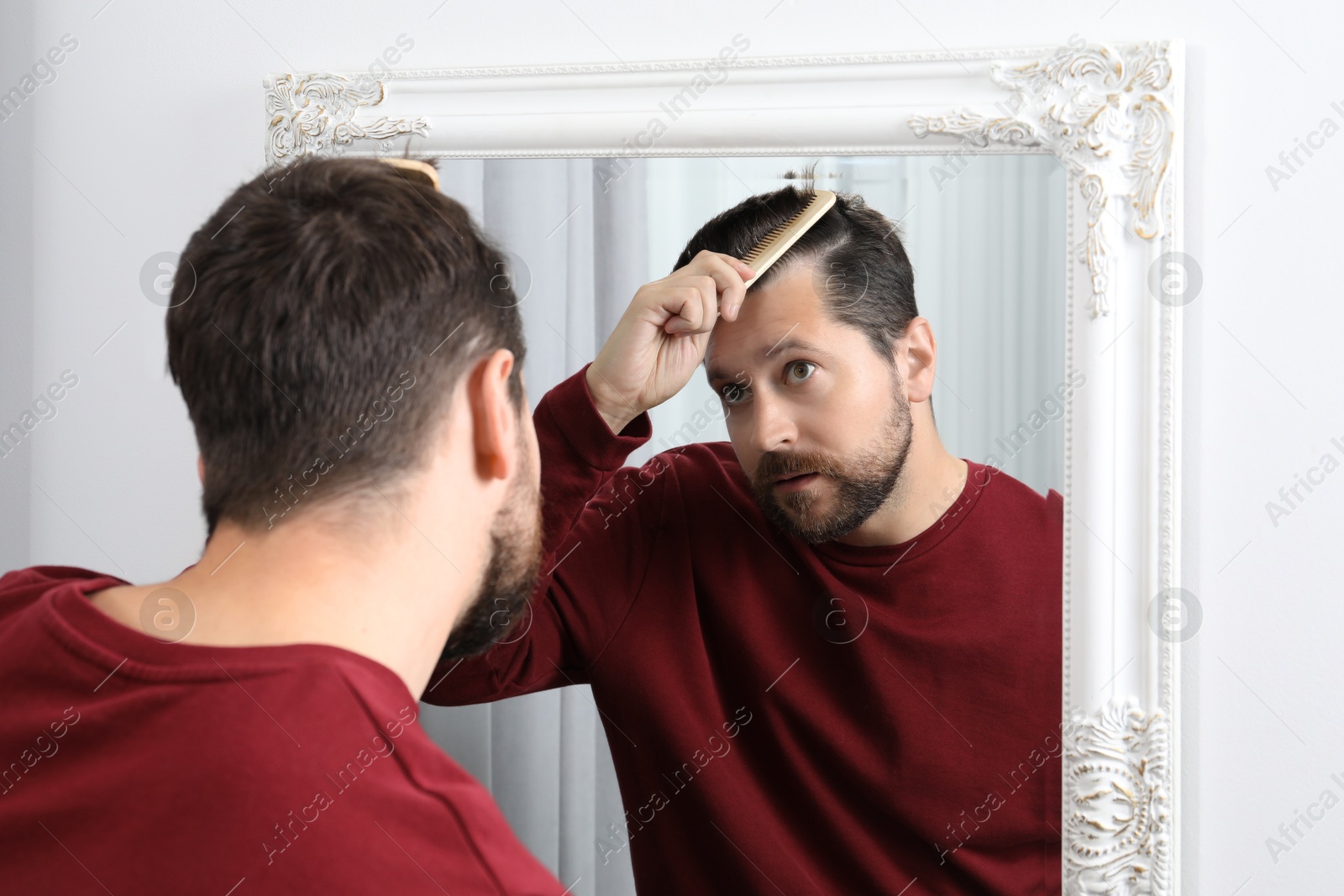 Photo of Man brushing his hair near mirror indoors. Alopecia problem