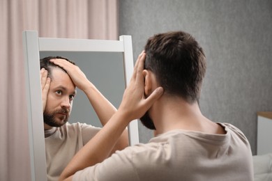 Man with hair loss problem looking at mirror indoors