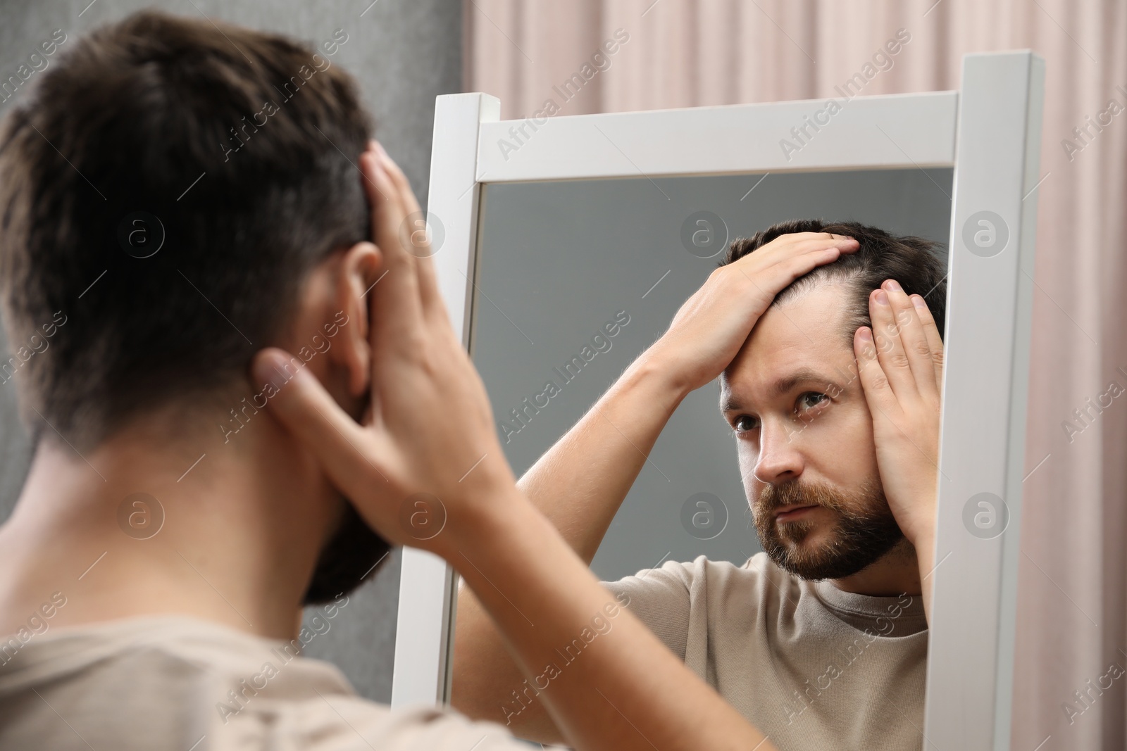 Photo of Man with hair loss problem looking at mirror indoors