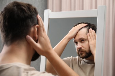 Photo of Man with hair loss problem looking at mirror indoors