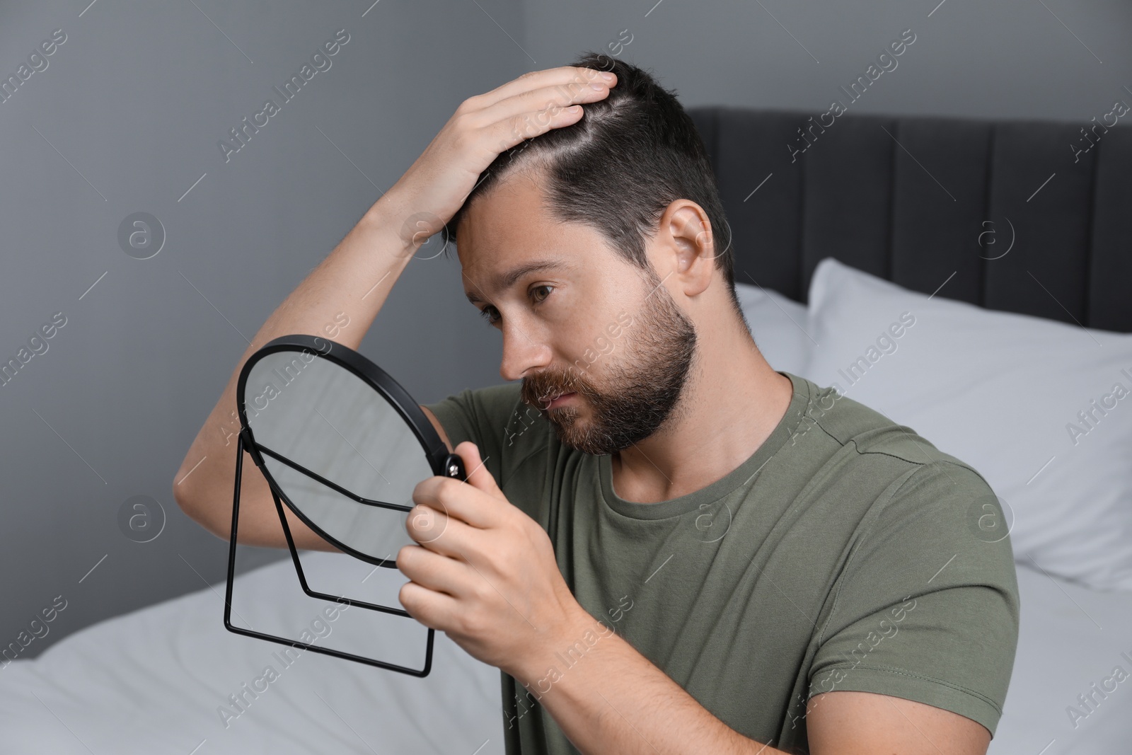 Photo of Man with hair loss problem looking at mirror indoors