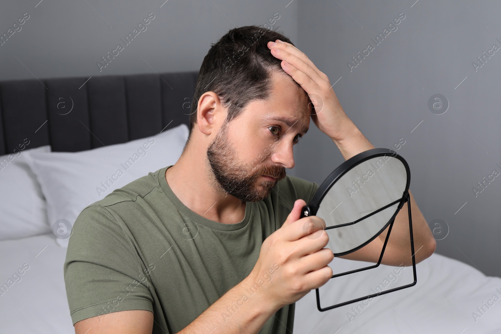 Photo of Man with hair loss problem looking at mirror indoors