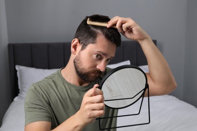 Photo of Man brushing his hair near mirror indoors. Alopecia problem