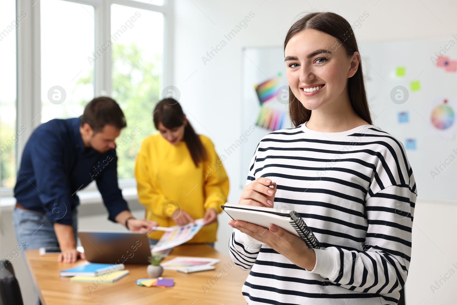 Photo of Portrait of happy young designer with notebook in office