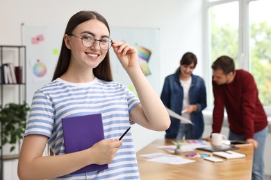 Portrait of happy young designer with notebook in office