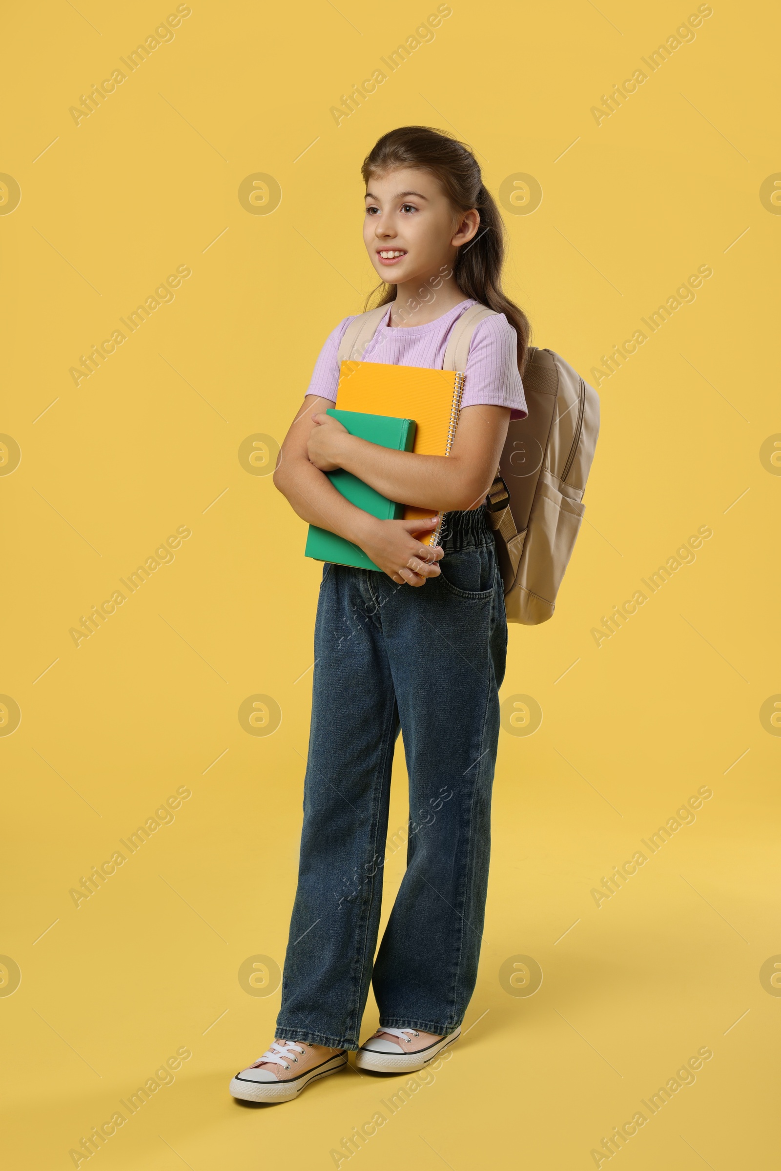 Photo of Girl with backpack and books on yellow background