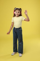 Cute girl listening to music on yellow background