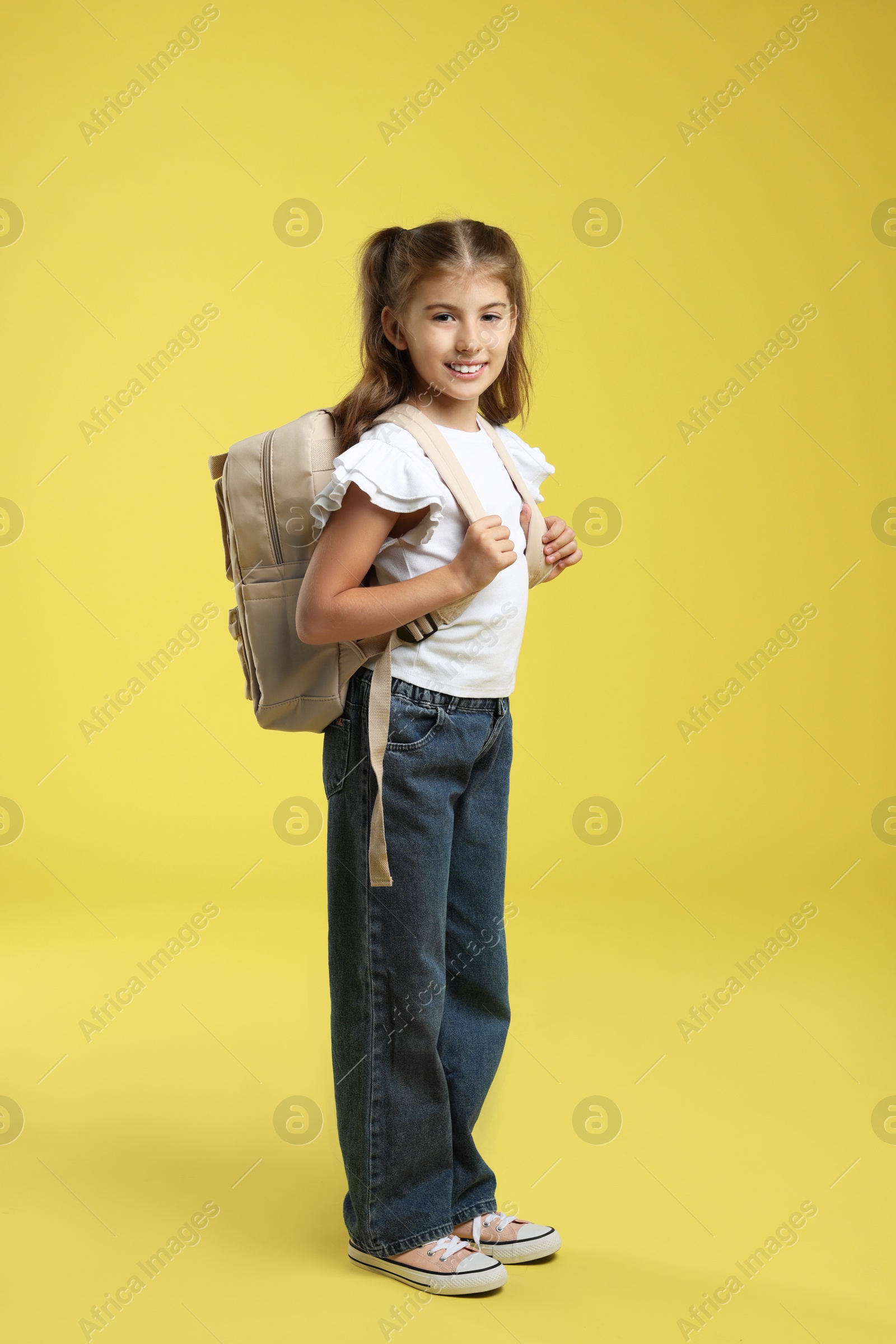 Photo of Positive girl with backpack on yellow background