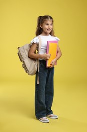 Photo of Positive girl with backpack and books on yellow background